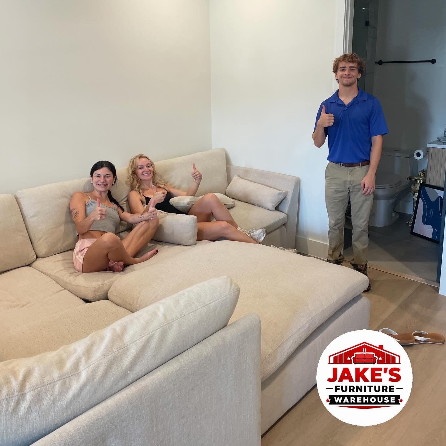 People sitting on a large beige sectional sofa in a living room with Jake's Furniture Warehouse logo.